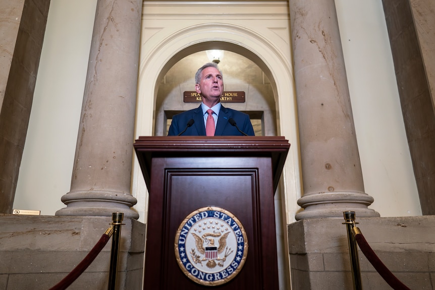 Kevin McCarthy stands at a podium, with a concrete archway behind him.