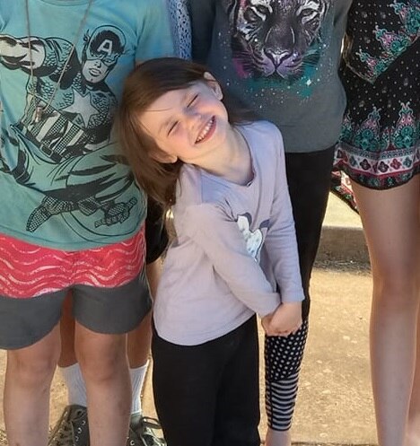 A young girl smiling with her eyes closed while clasping her hands together