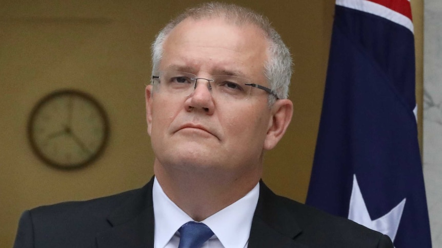Scott Morrison looks out over two microphones will making a speech in front of an Australian flag.