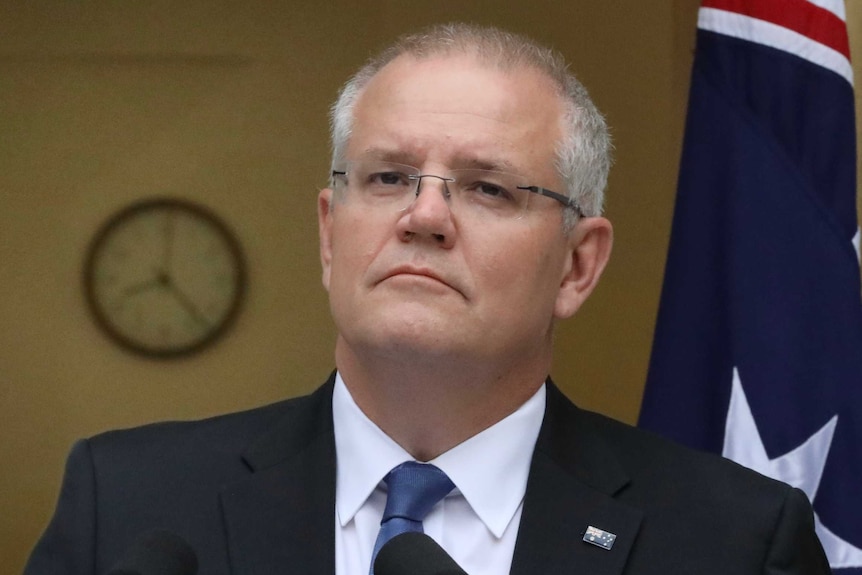 Scott Morrison looks out over two microphones will making a speech in front of an Australian flag.