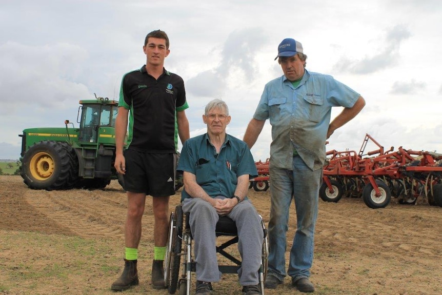 Dandaragan farmer, Ian Minty, sits in a wheelchair between John and grandson Gavin with tractors in the backgorund.