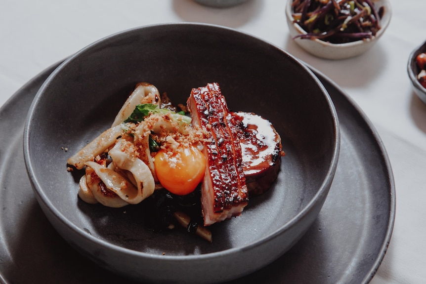 Wild boar belly and noodles sitting in a black bowl in a restaurant 