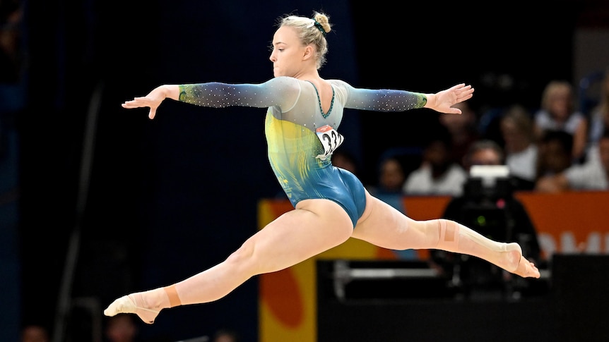 Gymnast Emily Whitehead of Australia jumps in the air, with arms and legs stretched out, in competition on the mat