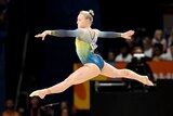 Gymnast Emily Whitehead of Australia jumps in the air, with arms and legs stretched out, in competition on the mat