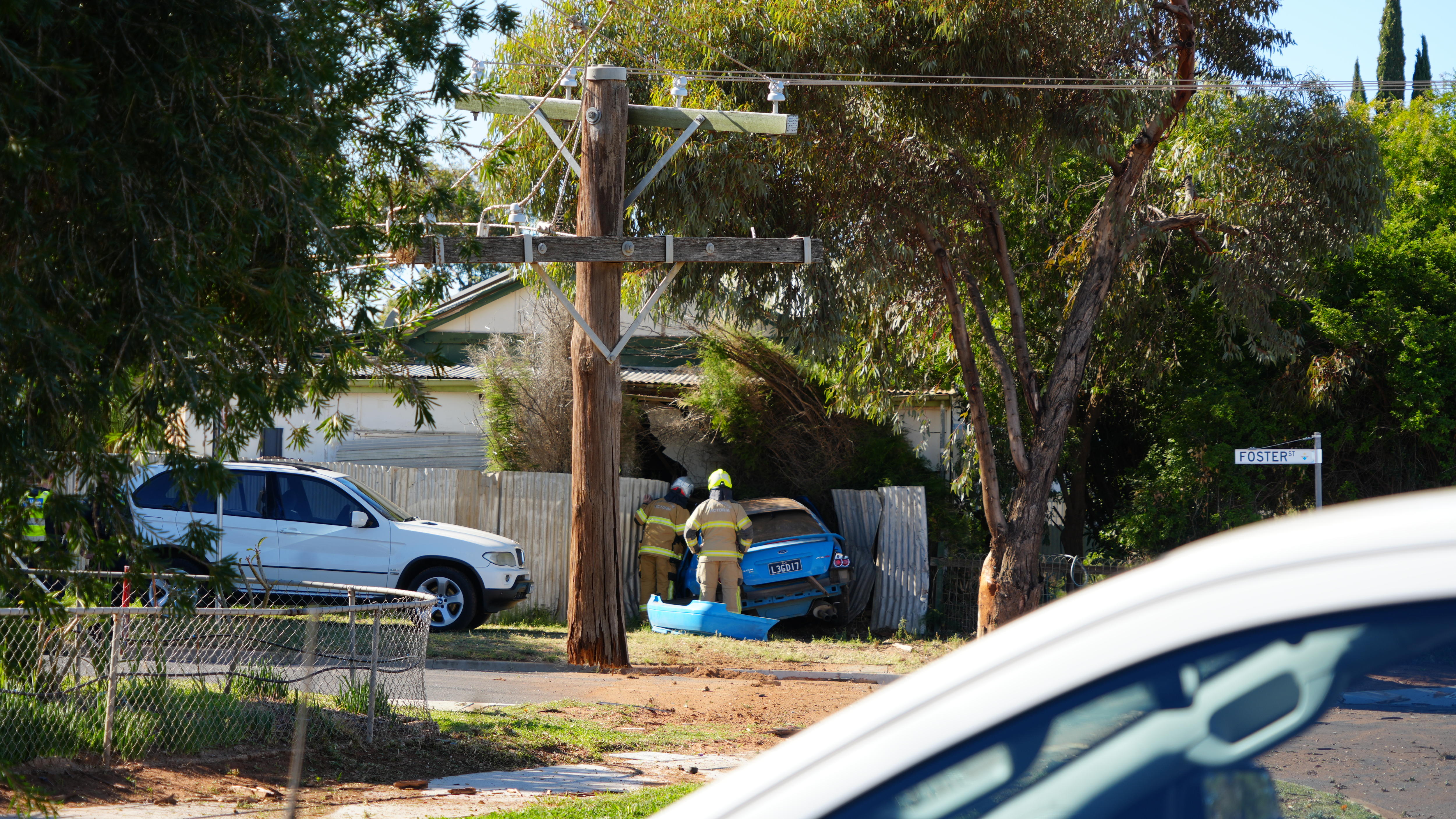 The scene of a crash where a blue car has drove through a wooden pole and into a house