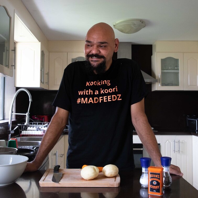 A bald man in a black shirt stands at his breakfast bar.