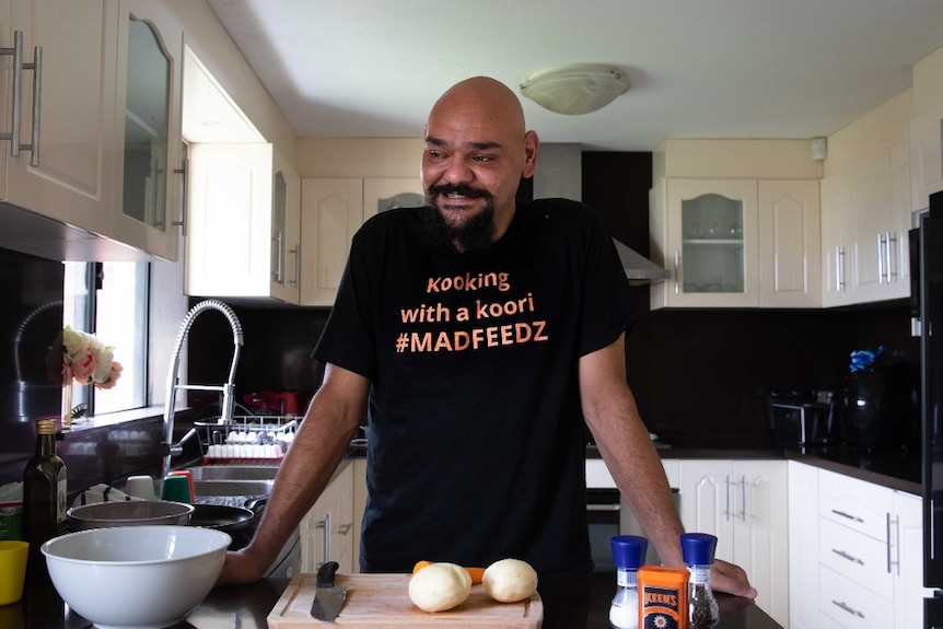 A bald man in a black shirt stands at his breakfast bar.