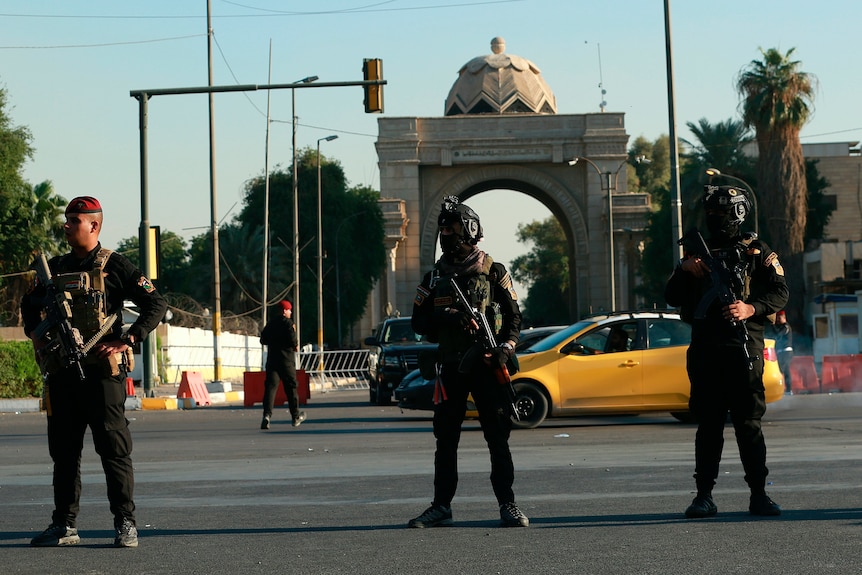 three armed soldiers stand outside the Green Zone in Baghdad during the day