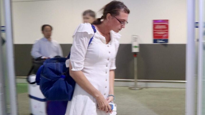 A woman wearing a long white shirt and glasses walks through an airport
