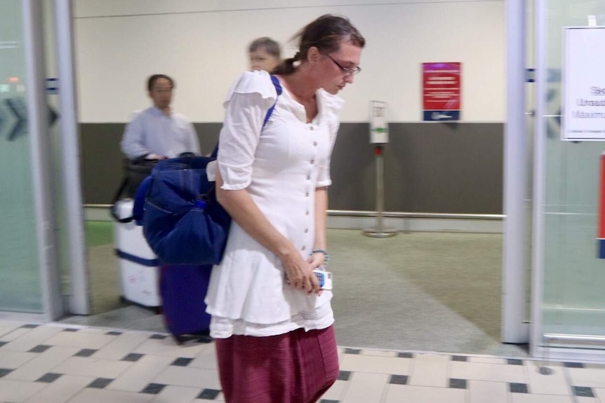 A woman wearing a long white shirt and glasses walks through an airport