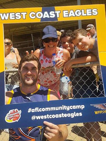 Jack Darling holds a large West Coast Eagles sign with fans behind him