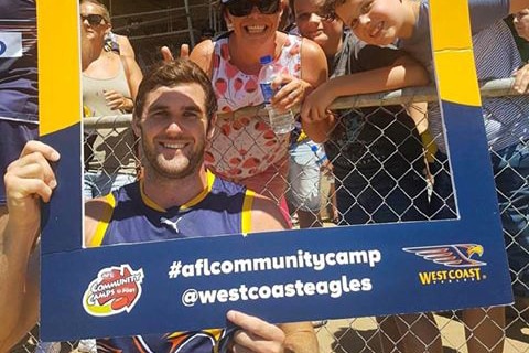 Jack Darling holds a large West Coast Eagles sign with fans behind him