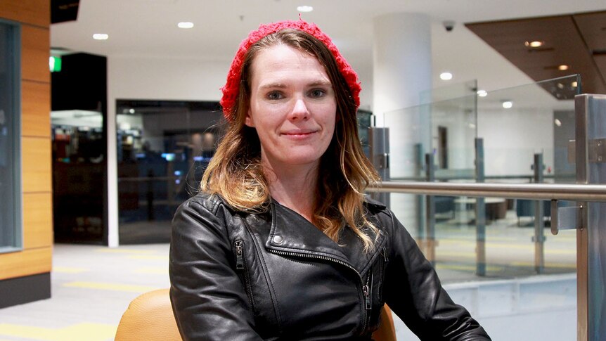 A woman in a red beanie and black leather jacket.