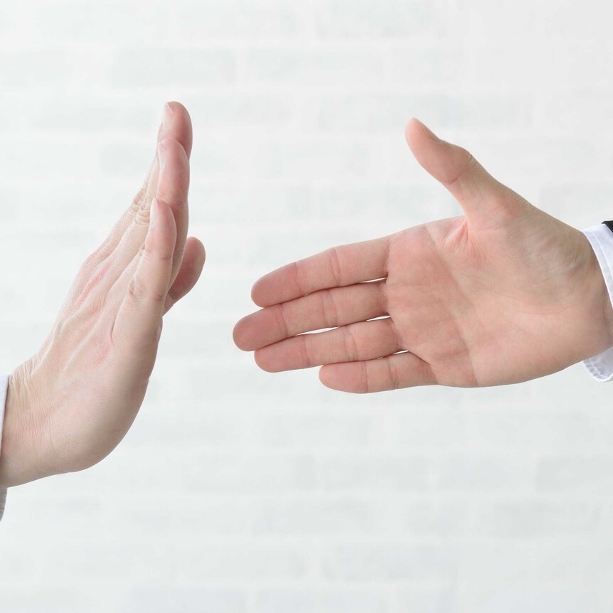 A picture of two hands, one offering a handshake and the other refusing by holding the hand up in a stop like manner