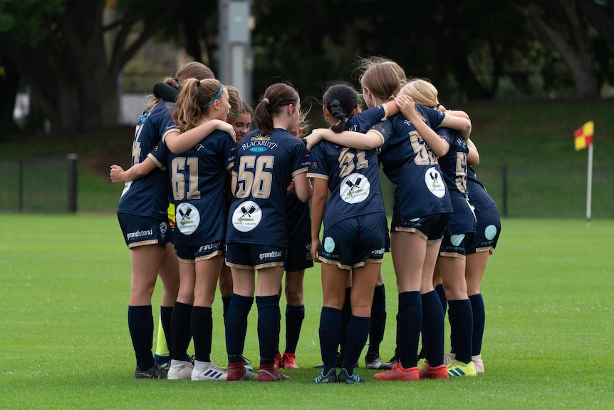 A group of girls huddled in a circle playing soccer