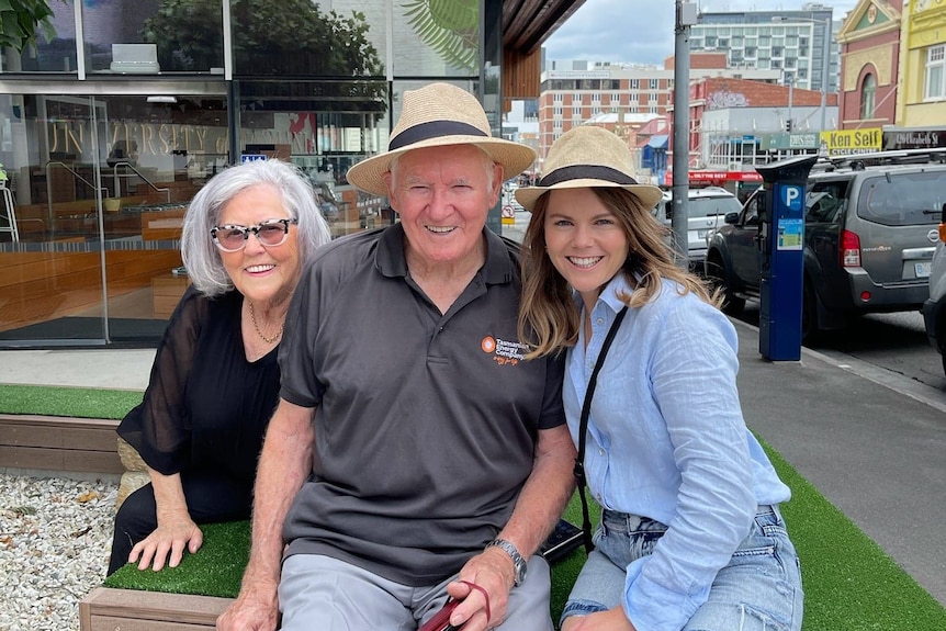 A young woman with her grandfather and grandmother smile at the camera.