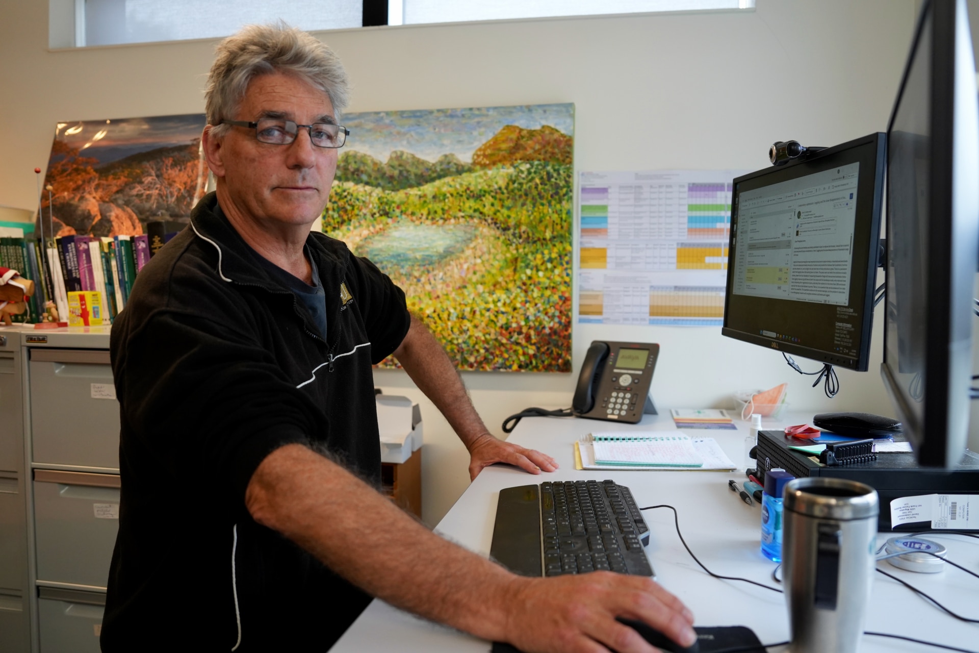 A man stands in front of his desk