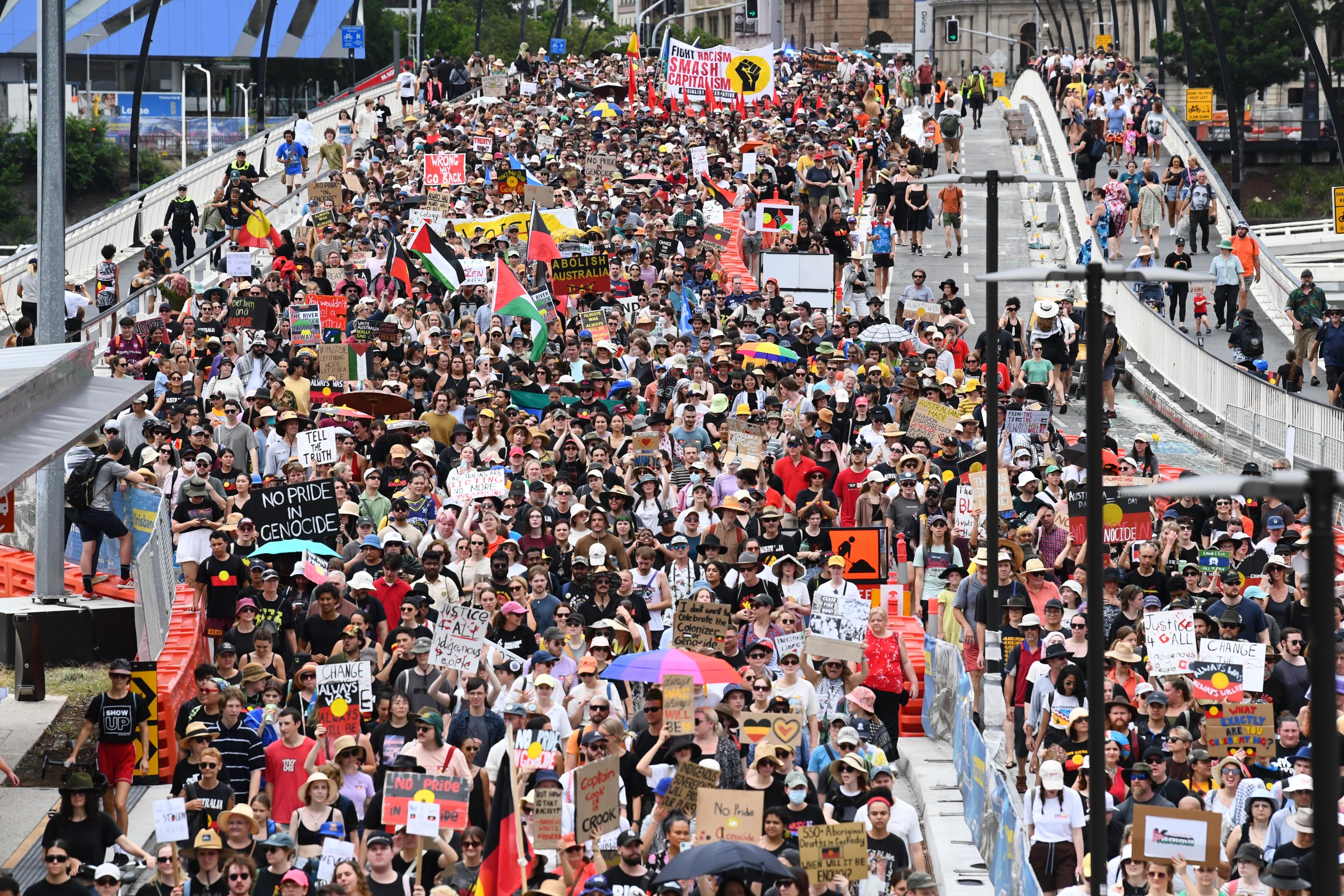Thousands of Invasion Day rally attendees march over a bridge in Brisbane