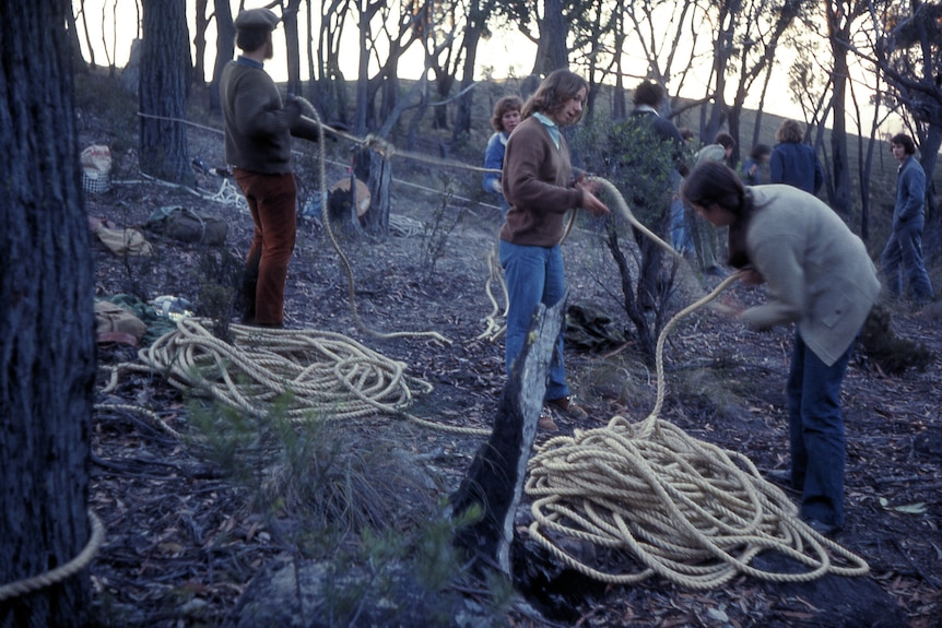 A group of people holding a large rope that is coiled on the ground in two piles.