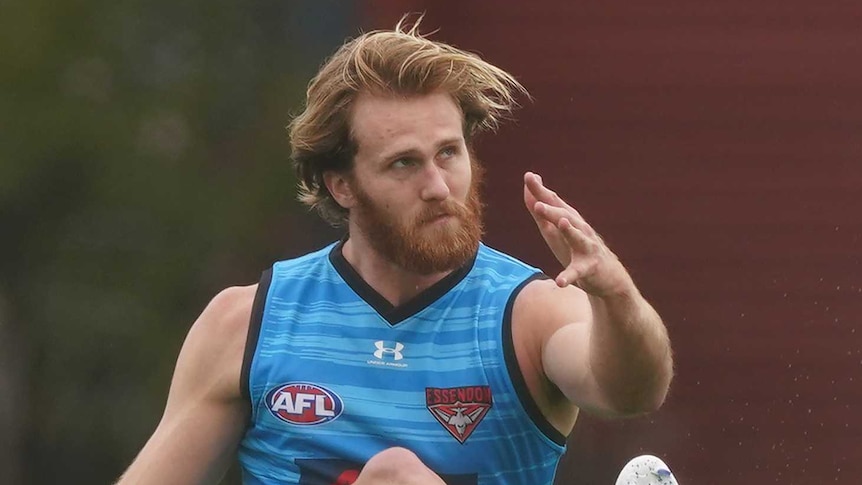 A bearded James Stewart completes his follow through after kicking an AFL ball at Essendon Bombers training.