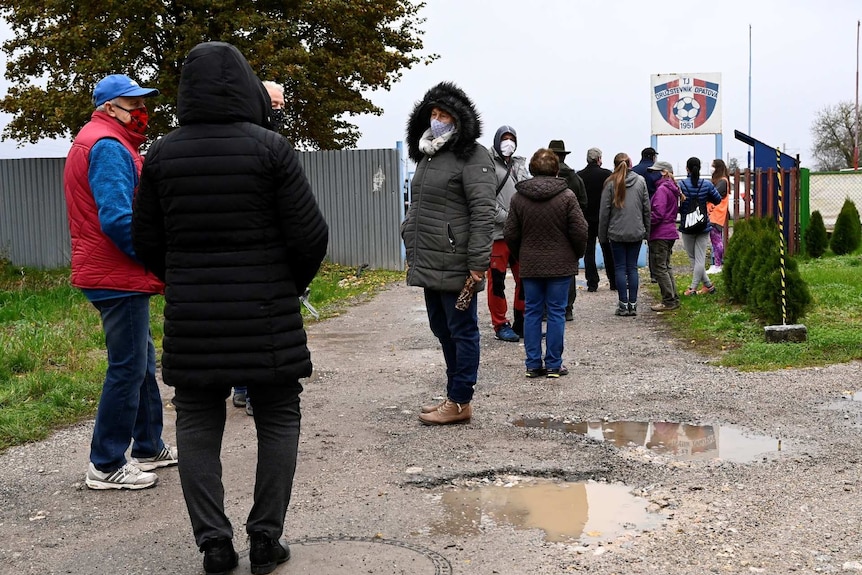 people line up on a dirt footpath outside a soccer ground in Slovakia