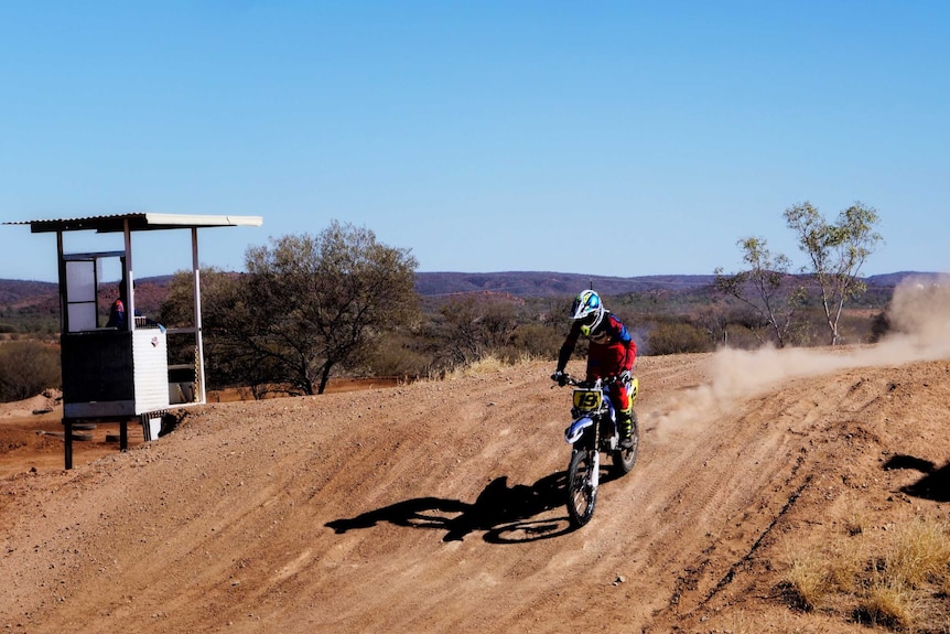 Photo of a boy riding a dirt bike down a red track with a dust trail