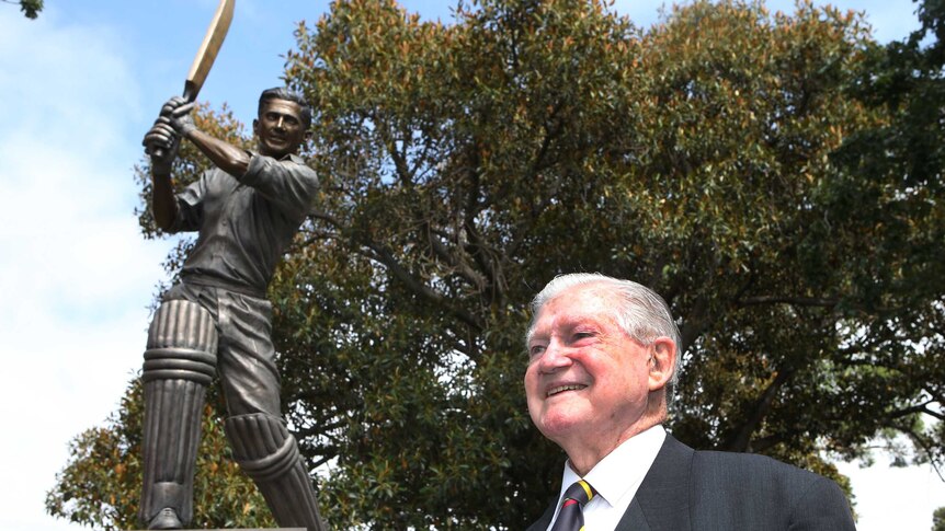 Former cricketer stands in front a statue of himself