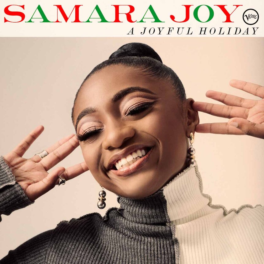 A smiling Samara Joy with her hands by her ears; she's wearing a black-and-white sweater