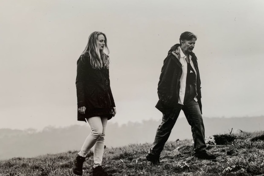 Black and white image of an older woman and younger woman walking in a field of grass.