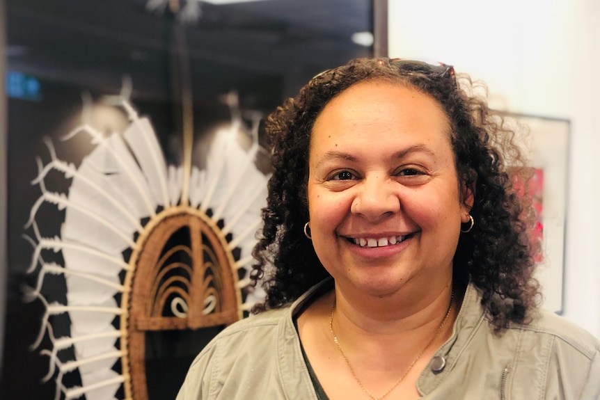 A woman looking at the camera and smiling with Indigenous artwork in the background