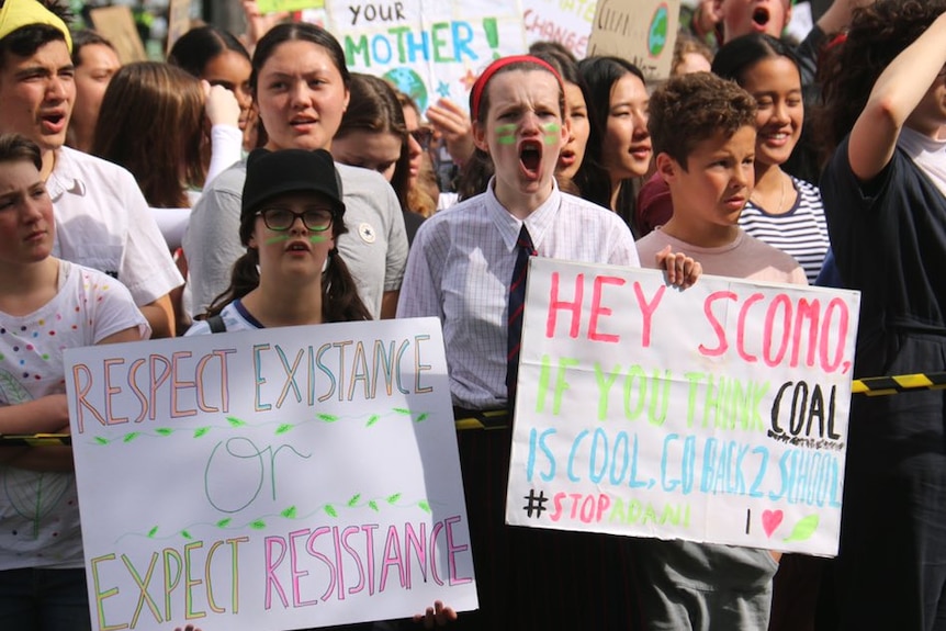 A young girl in school uniform stands in a crowd and shouts.