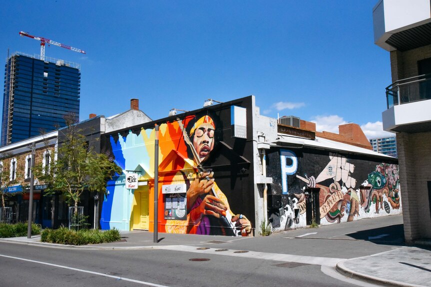 Exterior shot of a building covered with street art featuring the image of Jimi Hendrix playing guitar.