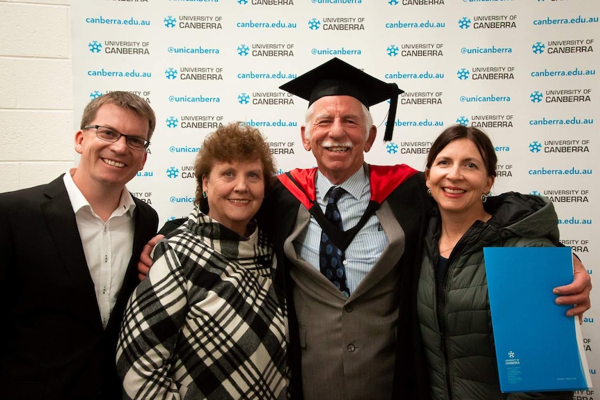 Peter Gately is posing for a graduation photo with his family.