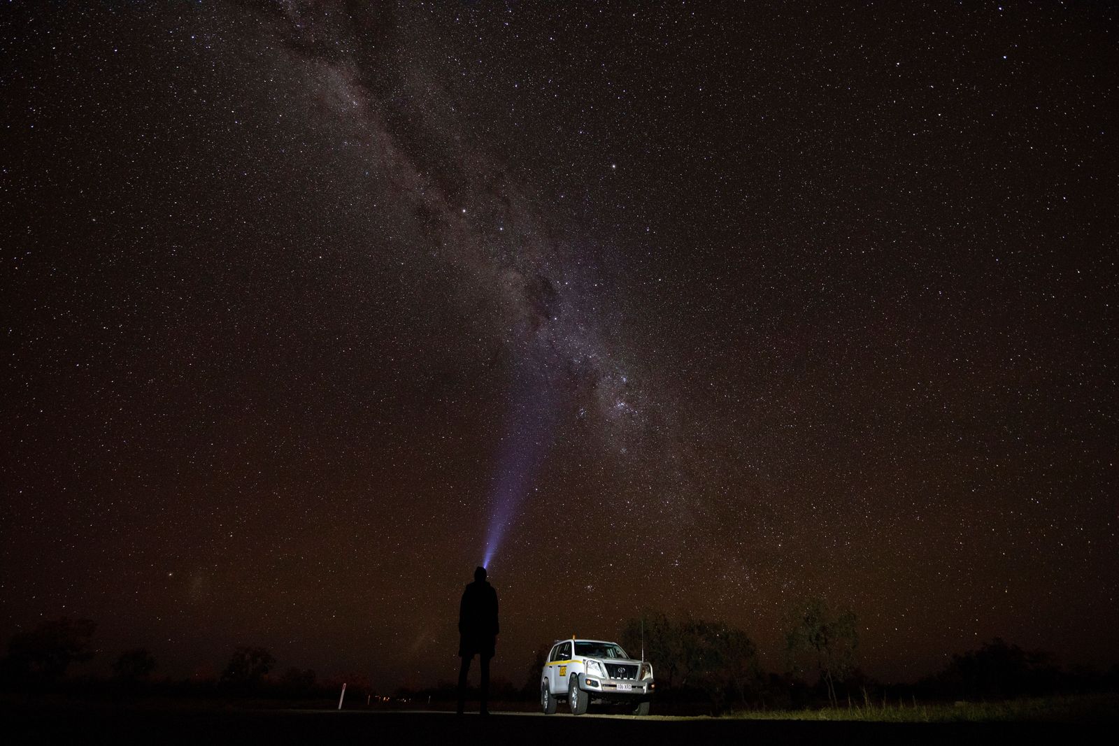 A stargazer points a torch at the night sky.