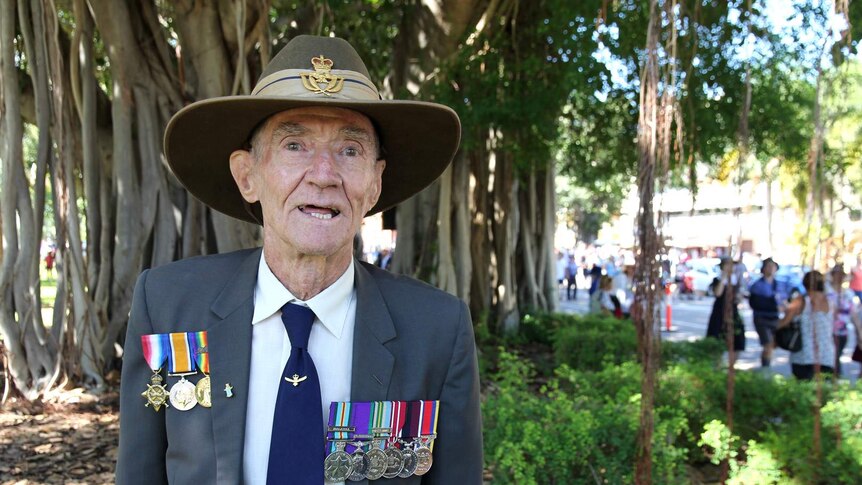 An older man wearing service medals stands in front of a tree on Townsville's Strand following an Anzac March.