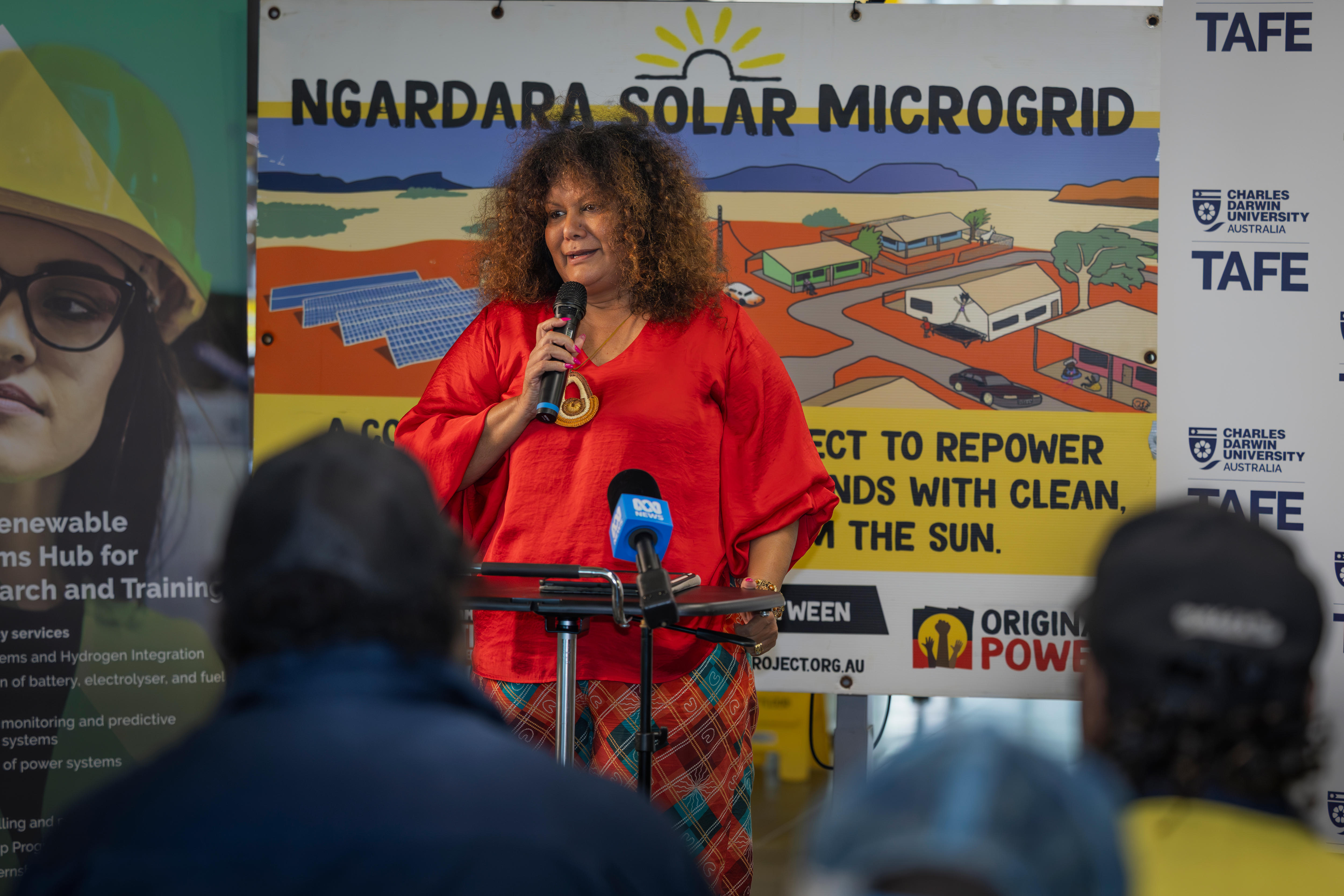 Mujer con pelo rizado sostiene el micrófono y habla a la multitud