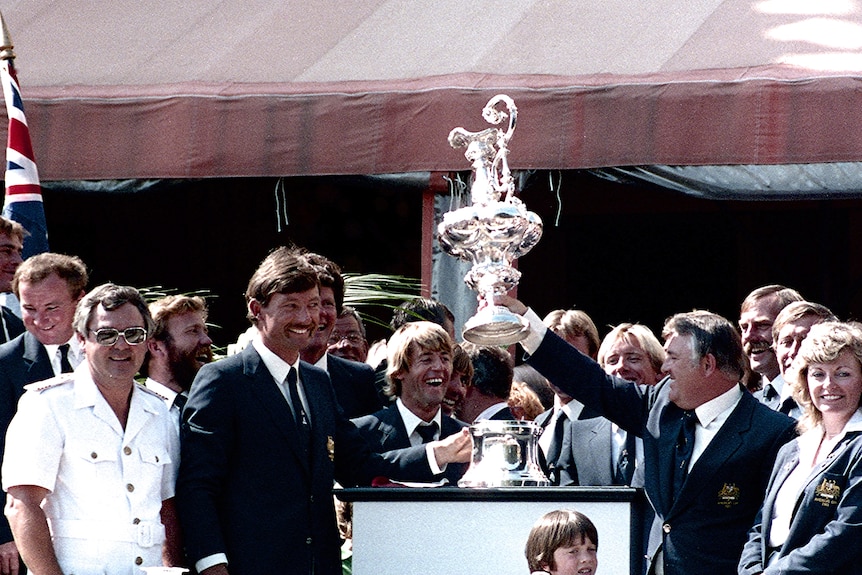A large group of smiling people gathered around a large trophy.