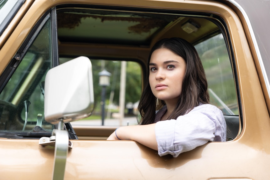 A TV still of Devery Jacobs, a Canadian Mohawk actor, sitting inside the cab of a truck. She has a determined expression.