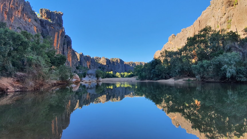 A still pool of water reflects trees and striking cliffs.