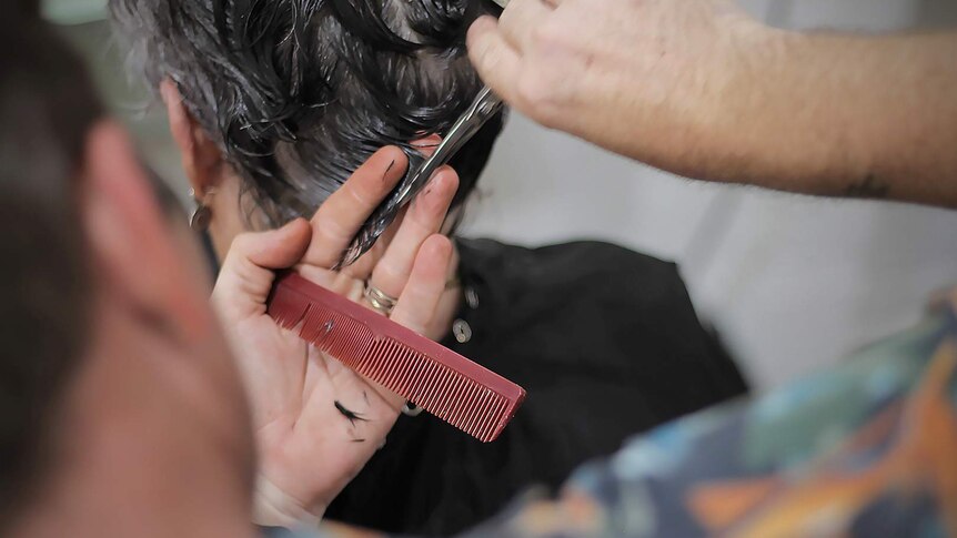 Close up of a male hairdresser cutting a woman's hair with a comb and scissors