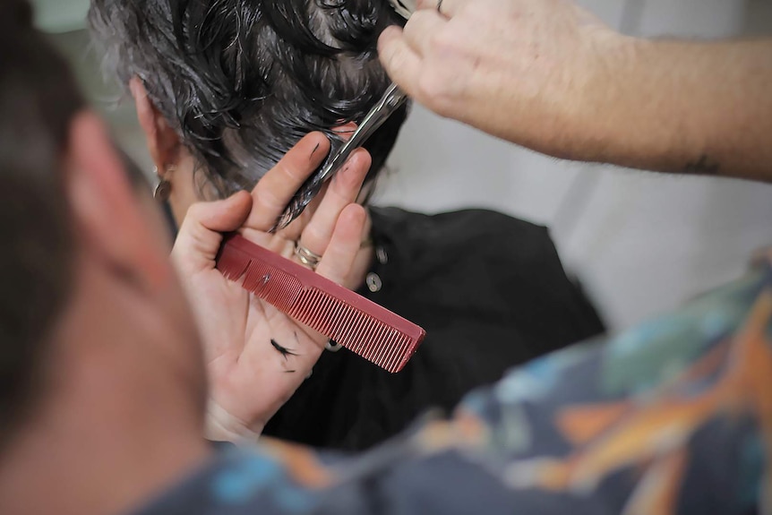 Close up of a male hairdresser cutting a woman's hair with a comb and scissors