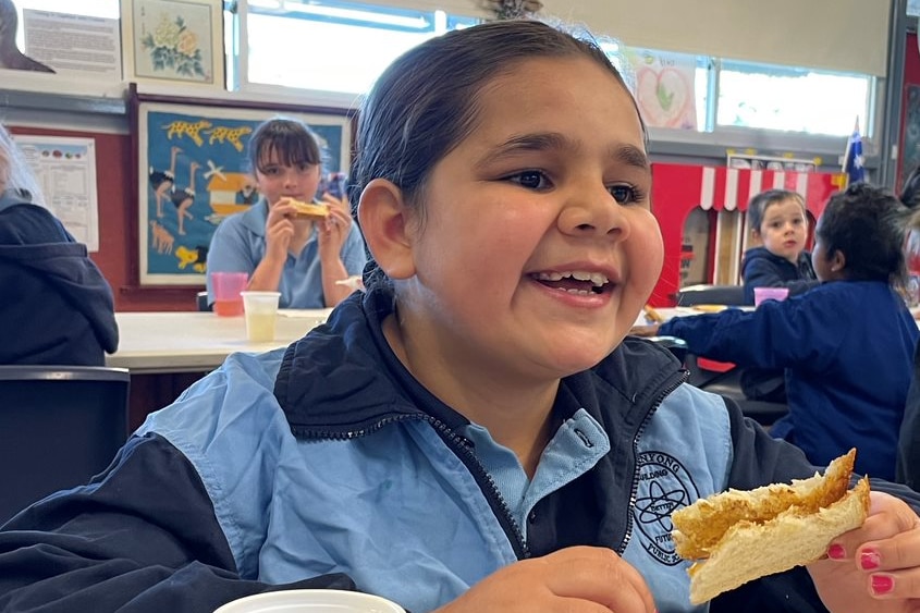 a young primary school aged girl eats toast and drinks milk