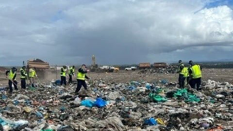 Seven police in hi-vos vests rake through piles of rubbish. 