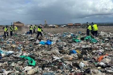 Seven police in hi-vos vests rake through piles of rubbish. 