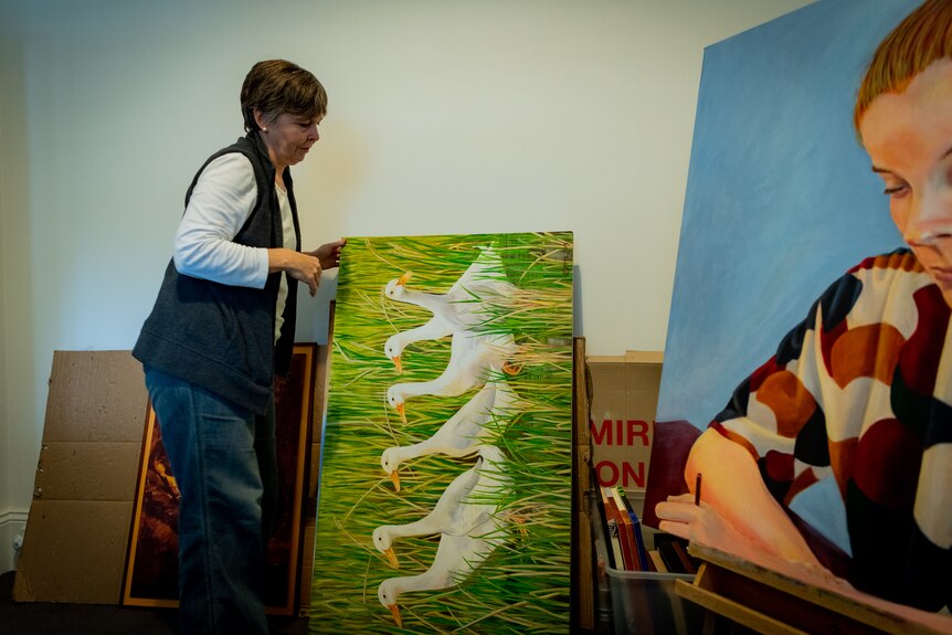Rebecca Smyth moves a painting of a row of white ducks closer to a large painting of a young woman.