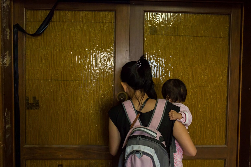 Layla, wearing a pink backpack, holds Tia as she opens the front door to her room.