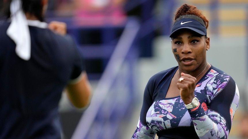 Serena Williams pumps her fist in celebration as she looks at her doubles partner (partly obscured) during a match.