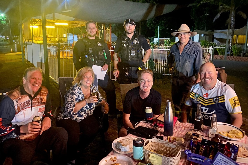 Police officers stand behind a party of happy people drinking in a holiday park.