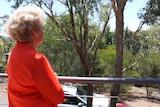 A woman looks off her balcony and into the bush.