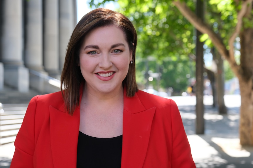 A woman wearing a red jacket standing in front of Parliament House